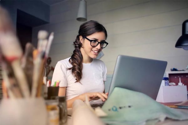 Woman wearing glasses working at laptop in bright office space with desk organizers and pendant lighting